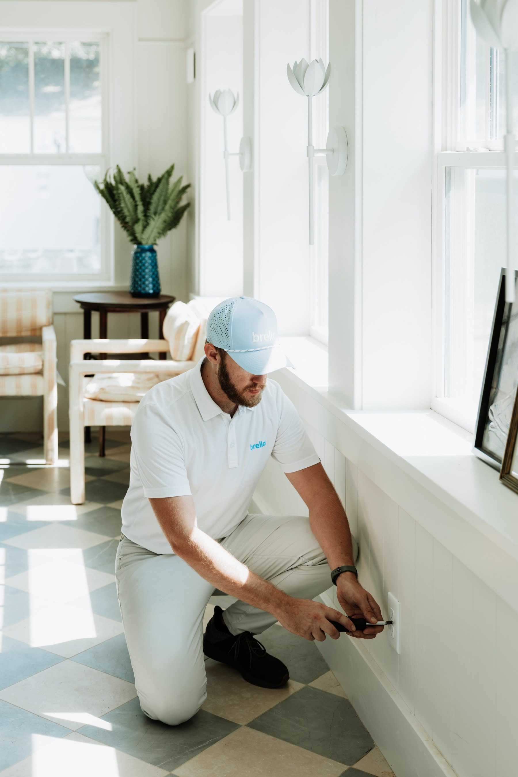 A Brella technician kneeling to test a wall outlet in a sunny room