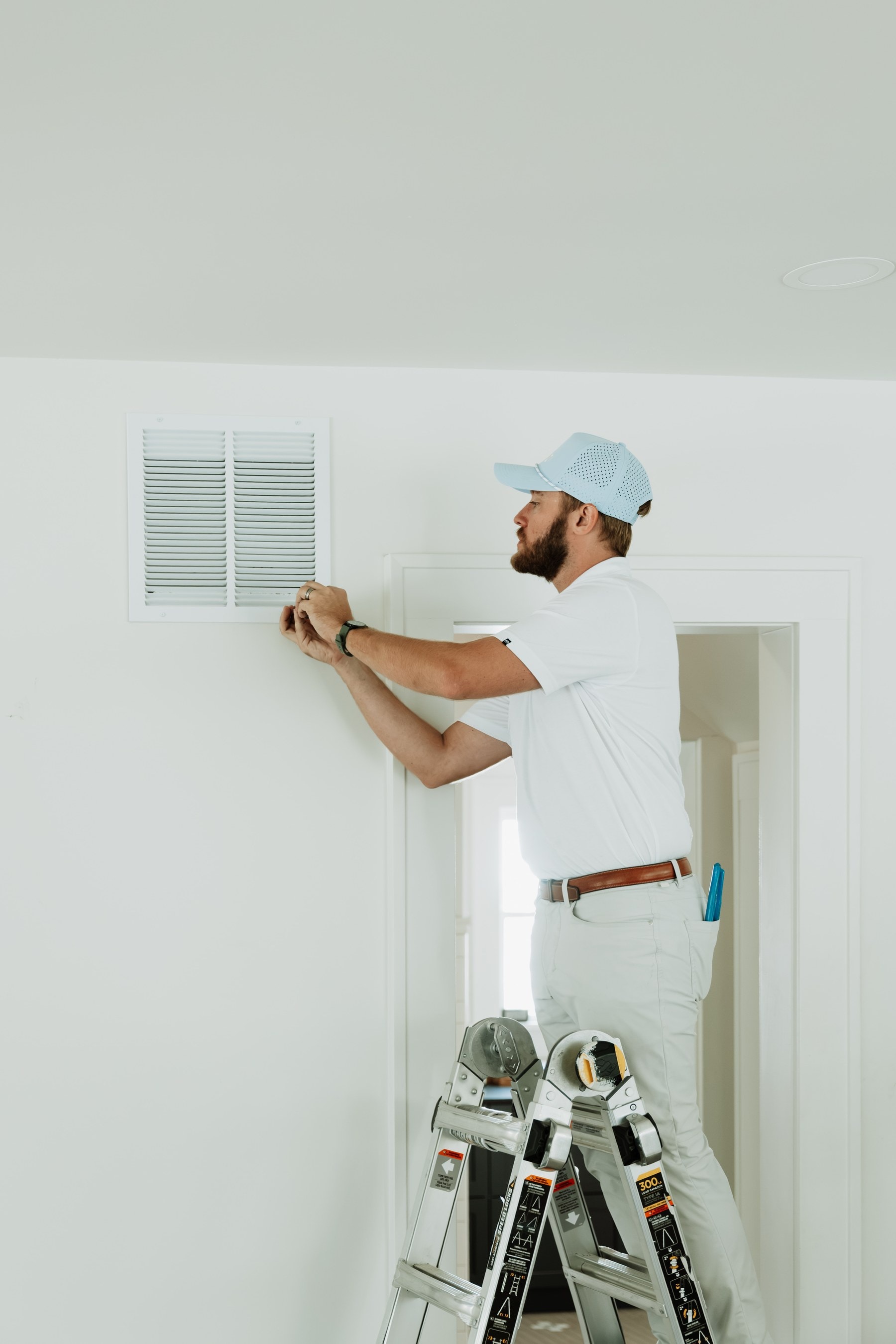 A Brella technician on a ladder checking a return-air vent cover
