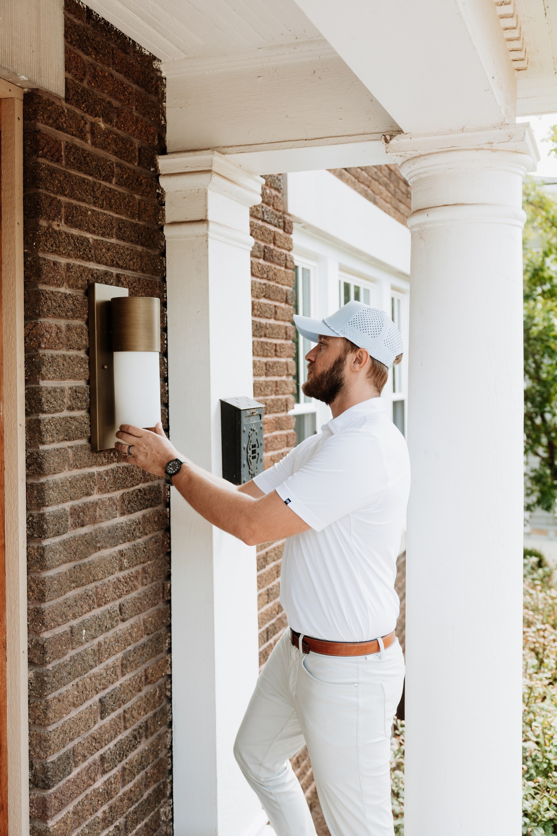 A Brella technician servicing a porch light on a brick entrance